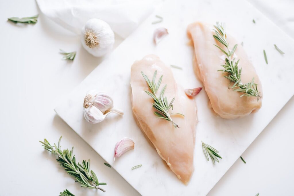 Top view of raw chicken breasts with rosemary and garlic, perfect for culinary ideas.
