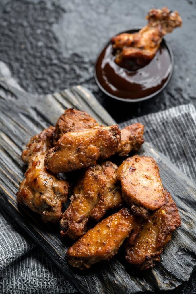 Appetizing barbecue chicken wings served with rich dipping sauce on rustic wooden board.